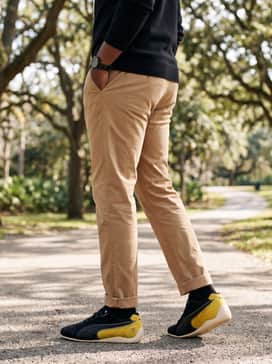 Scuderia Ferrari Speedcat Mens Sneakers – Tan or sand-colored chinos with a simple black crewneck sweater, allowing the bold yellow branding and streamlined silhouette of the shoes to serve as the focal point.
