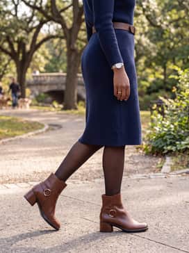 A navy blue ribbed knit sweater dress cinched at the waist with a matching brown leather belt and finished with sheer black tights for a polished office-to-dinner transition.