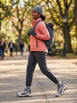Seasons Explore Nitro – Dark grey thermal hiking pants combined with a quilted coral-pink puffer jacket and a grey knit beanie for cold-weather trails.