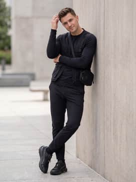 Seasons Voyage Nitro 3 Mens Running Shoes – A sleek urban techwear look with slim-fit water-resistant trousers, a black utility vest layered over a long-sleeve base layer, and a crossbody gear bag.