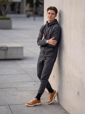 Session Se – A monochromatic charcoal grey tech-fleece tracksuit featuring tapered bottoms and a zip-up hoodie, allowing the burnt orange sneakers to serve as a vibrant pop of color.