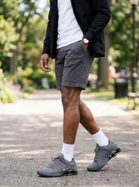 Dark grey chino shorts worn with a crisp white crewneck t-shirt and an unbuttoned black utility shirt.