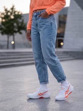 A street-ready ensemble with light-wash tapered denim jeans, an oversized cropped hoodie in a matching bright orange, and a minimalist white crossbody bag.