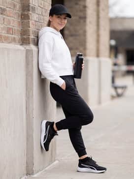Tapered black joggers and a cropped white oversized hoodie, accessorized with a sporty baseball cap for a comfortable and stylish post-workout ensemble.