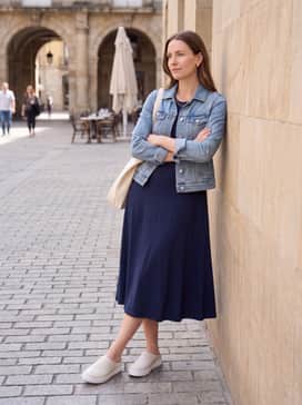 Soft 60 – A navy blue midi-length jersey sun dress layered with a light denim jacket and gold minimalist jewelry for a relaxed weekend brunch.