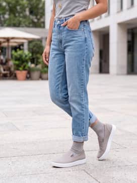 Soft 60 – Light-wash boyfriend jeans with a cuffed hem, paired with a soft cream cashmere sweater and a delicate gold pendant necklace.