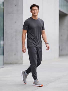 Softride Enzo 5 Wide – Dark charcoal slim-fit joggers paired with a matching moisture-wicking grey performance tee and an orange-accented fitness tracker for a cohesive gym look.