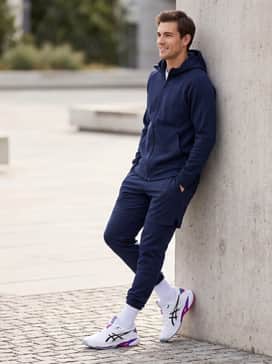 A clean athleisure outfit pairing navy blue tech-fleece joggers with a matching zip-up hoodie, creating a cohesive backdrop for the vibrant purple and pink heel details.