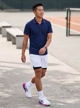 A professional court ensemble featuring crisp white moisture-wicking shorts and a fitted navy blue performance polo with magenta piping to echo the shoe's accents.