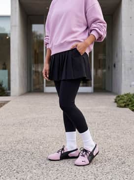 Style with a black pleated tennis skirt, a matching baby pink oversized crewneck sweatshirt, and white crew socks to lean into the sporty-feminine aesthetic.