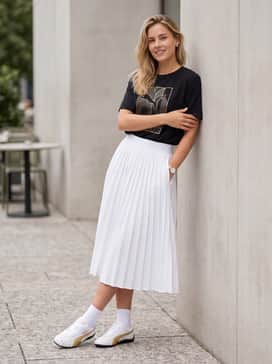 A white pleated tennis skirt and a tucked-in oversized graphic tee in black and gold for a playful, athletic-inspired outfit.