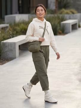 High-waisted olive cargo pants paired with a cropped cream graphic hoodie and a structured nylon crossbody bag for a modern utilitarian look.