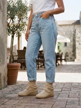 Light-wash distressed boyfriend jeans with a slight cuff, styled with a tucked-in white graphic tee and an olive green utility jacket.