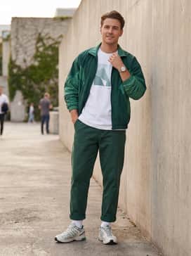 Olive green cargo pants with cinch-cords at the ankles, a simple white graphic tee, and a vintage-style nylon track jacket in matching green tones.