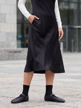 A black satin midi slip dress layered over a slim-fit white turtleneck for a balanced feminine-meets-sporty aesthetic.