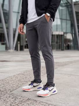 A clean athleisure outfit consisting of slim-fit charcoal joggers, a heavyweight white cotton tee, and a black unlined windbreaker for a sleek street-ready appearance.