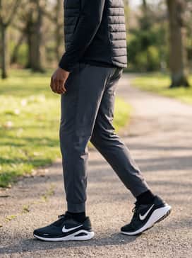A casual urban outfit combining slim-fit dark charcoal jeans with a simple black long-sleeve crewneck and a matte black quilted puffer vest for a sporty, everyday aesthetic.