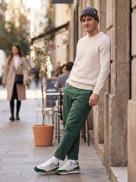 Tapered beige chinos with a clean hem, a minimalist black crewneck sweatshirt, and a lime green beanie that subtly picks up the neon accents on the shoe's tongue and heel.