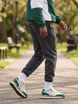 Dark charcoal grey tech-fleece joggers, a color-blocked windbreaker in matching forest green and white, and high-quality white crew socks for a modern streetwear silhouette.