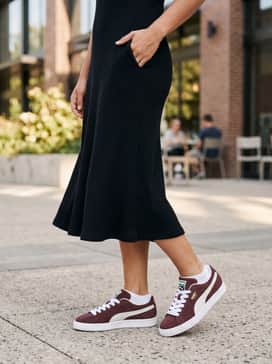 A black ribbed midi dress layered with an oversized olive green bomber jacket and gold jewelry to complement the shoe's gold foil branding.