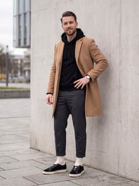 Dark grey tailored joggers combined with a high-quality black hoodie and a structured camel overcoat to achieve a high-fashion streetwear aesthetic.