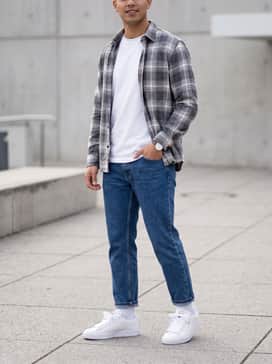 Baggy light-wash distressed denim jeans with a tucked-in graphic t-shirt and an unbuttoned flannel shirt for a classic 90s-inspired look.