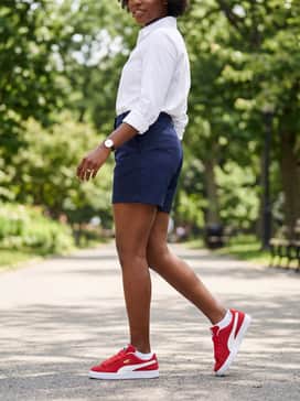 Navy blue tailored shorts and a crisp white button-down shirt for a preppy, polished outfit that lets the red sneakers pop.