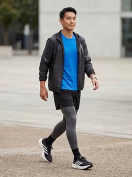 A pair of charcoal grey moisture-wicking compression tights layered under black mesh running shorts, paired with a fitted electric blue performance tech tee and a lightweight reflective windbreaker for early morning visibility.