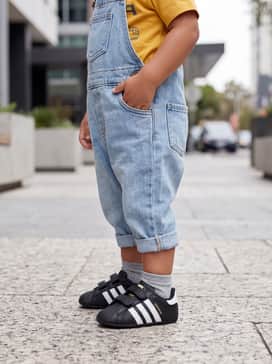 Light-wash denim overalls paired with a bright graphic t-shirt and a small knit beanie.