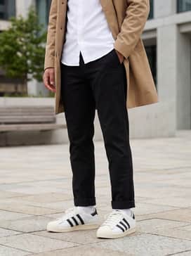 Slim-fit black chinos paired with a crisp white button-down shirt and a tan trench coat for a smart-casual office transition.