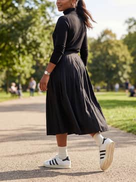 A neutral-toned pleated midi skirt and a fitted black turtleneck sweater for a chic, feminine take on sporty heritage.