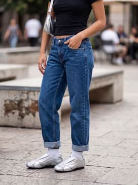 Baggy low-rise indigo denim jeans with a cropped black graphic baby tee and a small silver shoulder bag to lean into a Y2K-inspired street aesthetic.