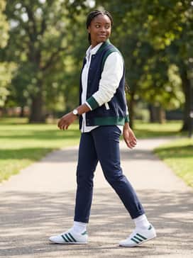 Slim-fit navy chinos worn with a crisp white button-down shirt and a varsity jacket featuring green accents for a classic collegiate vibe.