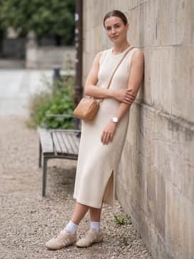 A cream-colored knit midi dress with a side slit, accessorized with a small leather crossbody bag in a matching tan shade for a sophisticated monochrome outfit.