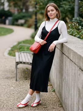 A black midi-length slip dress worn over a thin white turtleneck, accessorized with a red shoulder bag to echo the shoe stripes.