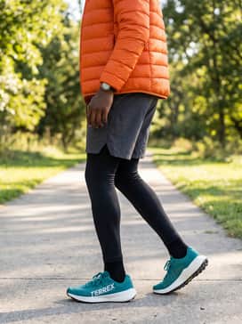 A cold-weather trail setup including black thermal compression tights under charcoal grey hiking shorts, paired with a bright orange puffer jacket for high-visibility.
