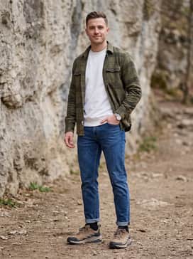 A casual weekend ensemble pairing tapered indigo denim jeans with a crisp white crewneck sweatshirt and an unbuttoned olive green plaid flannel shirt for a rugged yet refined vibe.