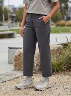 An urban gorpcore ensemble with charcoal wide-leg technical trousers, a boxy white graphic t-shirt, and an unzipped olive utility vest.