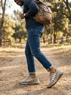 A rugged casual style with slim-fit dark wash denim, a mustard yellow flannel button-down layered over a white ribbed tank, and a canvas roll-top backpack.