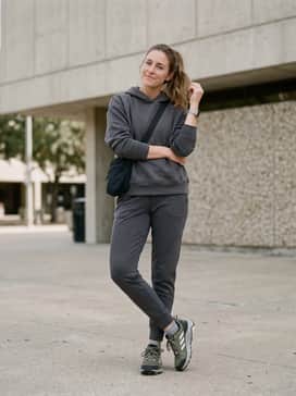 A relaxed travel outfit consisting of charcoal grey tapered joggers, a matching oversized hoodie, and a sleek black crossbody bag for a coordinated airport-ready look.