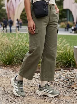 Wide-leg olive cargo trousers worn with a cream-colored cropped fleece pullover and a black technical crossbody bag for a trendy gorpcore aesthetic.