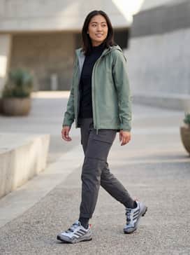 A technical gorpcore ensemble consisting of charcoal ripstop cargo trousers, a fitted black base layer, and a sage green GORE-TEX rain shell.