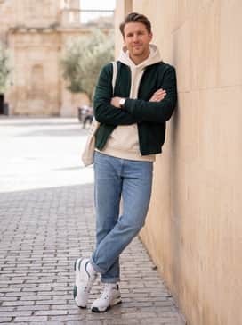 A sophisticated streetwear ensemble pairing light-wash straight-leg denim with an oversized cream-colored hoodie and a structured wool bomber jacket in forest green.