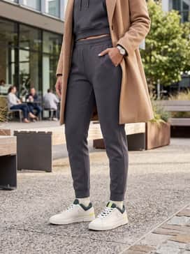 Style with high-waisted charcoal grey joggers and a matching cropped hoodie under a tan overcoat for a sleek, monochromatic athleisure look.