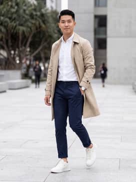 A smart-casual look featuring tapered navy chinos, a tucked-in white oxford shirt, and a lightweight beige trench coat for a sophisticated city vibe.