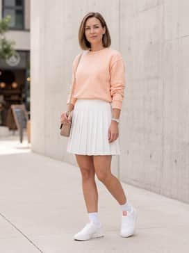 A pleated white mini skirt worn with a pastel peach crewneck sweatshirt to highlight the shoe's subtle tongue detailing.