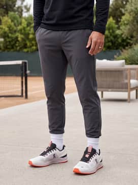 Tapered charcoal technical joggers paired with a fitted black quarter-zip pullover and a vibrant orange cap to echo the shoe's outsole.