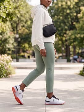 High-waisted sage green yoga leggings styled with an oversized off-white hoodie and a sleek black crossbody bag for a high-end gym-to-brunch transition.