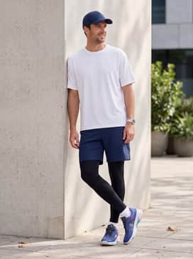 The Roger Pro Fire Clay – Navy blue athletic shorts over black performance leggings, topped with a white graphic tech-tee and a matching blue baseball cap for a modern gym look.