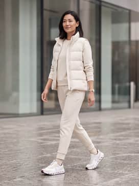 A monochromatic cream sweatsuit with a tailored puffer vest for a high-end airport lounge aesthetic.